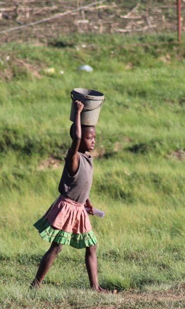Girl walking in fields of South Arica carrying bucket on her head